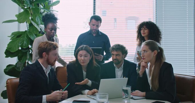 Multi-ethnic group of people listening carefully to woman sitting in front of computer. Consulting together about difficult decision for business company. Working together. Looking at laptop monitor.