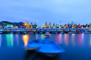 Jangnim-dong, Saha-gu, Busan, South Korea - June 8, 2019: Long exposure and night view of two fishing boats moored on the sea with motion against houses with colorful light at Jangnim Port