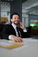 A man in a suit is talking on his cell phone. He is smiling and he is enjoying the conversation