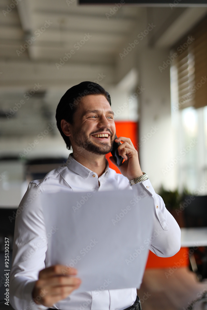 Poster a man is talking on his cell phone while holding a piece of paper. he is smiling and he is in a good