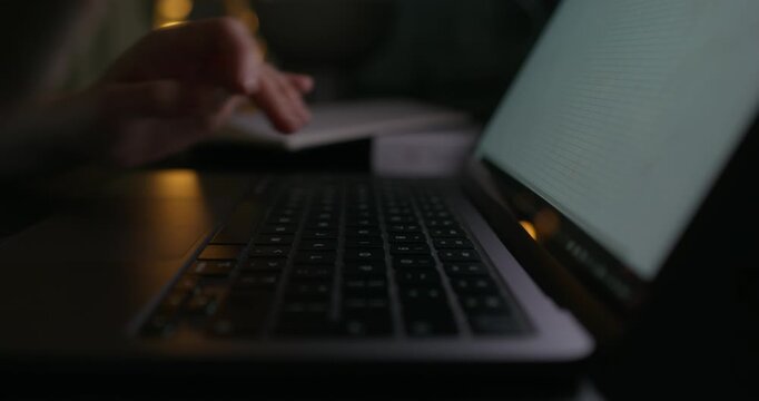 A woman typing on a laptop keyboard while sitting at a table in the dark. Close-up of her hands, an unrecognizable person.
