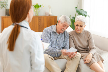 Female doctor examining older senior couple in doctor office or at home. Old woman man patient and doctor have consultation in hospital room. Medicine healthcare medical checkup. Visit to doctor