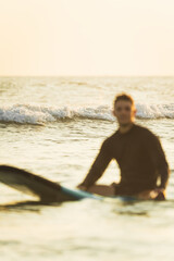 Out-of-focus surfer resting on his surfboard in the ocean