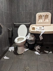 The interior of very dirty, filthy and messy public washroom with overflowing trash can and toilet...