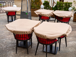 Unused tables at an outdoor cafe covered with covers