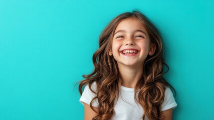 Happy young girl with long straight hair, laughing joyfully against a teal background.