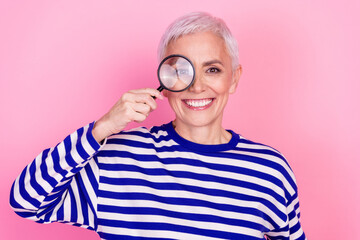 Photo of charming lovely senior woman wear striped trendy clothes hold magnifier isolated on pink...