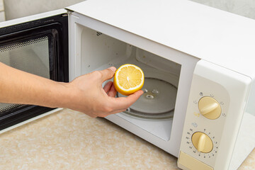 Cleaning microwave oven with lemon. Man puts half lemon in the microwave