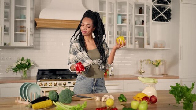 Portrait of joyful vegetarian woman in kitchen, lady throwing paprika in air. Healthy nutrition and good mood, stay slender and beautiful when eating fresh organic vegetables, pretty African girl