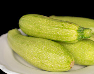 Four ripe zucchini with ceramic plate, macro, isolated on black background.