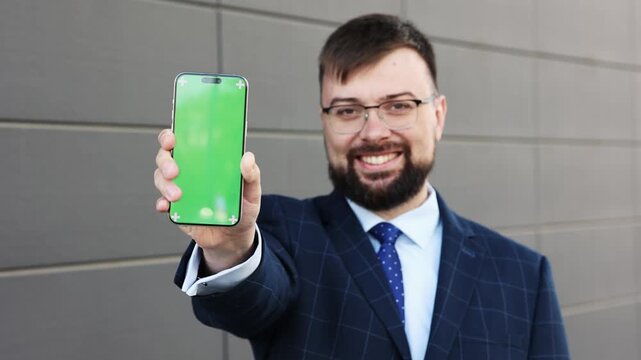 Close-up man businessman suit smiling looking directly camera using smartphone background wall. man's hand holds smartphone green screen layout. Using apps your mobile phone. chroma key mockup 