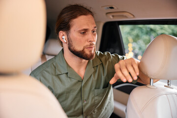 Young man with earbuds in car looking thoughtful