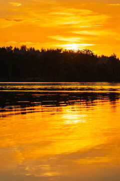 Zach&oacute;d słońca nad jeziorem z odbiciem w lustrze wody