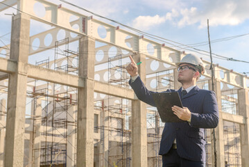 Asian adult foreman stands in front of the construction inspecting a construction project with determination. Engineer inspects construction.