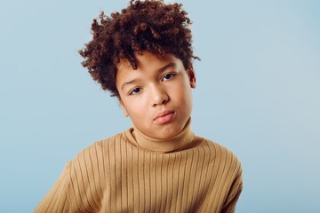 Young african american boy posing confidently in a warm turtle neck sweater against a bright blue background