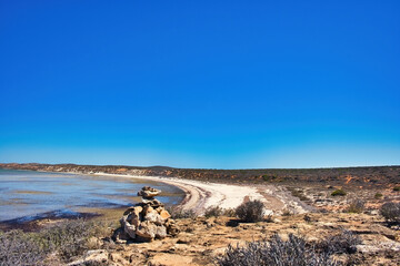 Deserted beach, lagoon and outback vegetation at Whale Bone Point, Denham, Western Australia. Small cairn in the foreground
