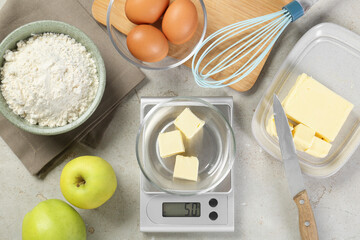 Kitchen scale with bowl of butter and other products on grey table, flat lay