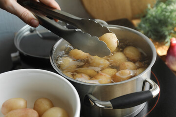 Woman putting potato into pot on stove, closeup