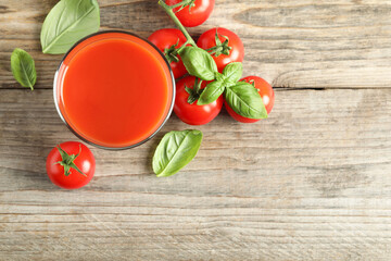 Tasty tomato juice in glass, basil leaves and fresh vegetables on wooden table, flat lay. Space for...
