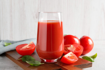 Tasty tomato juice in glass, basil leaves and fresh vegetables on light grey table