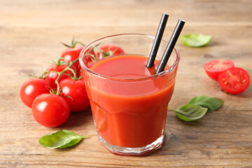Tasty tomato juice in glass, basil leaves and fresh vegetables on wooden table