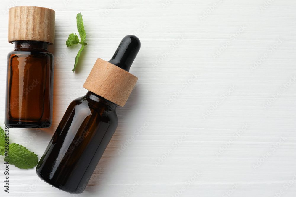 Wall mural bottles of mint essential oil and fresh leaves on white wooden table, top view. space for text