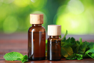 Bottles of mint essential oil and fresh leaves on wooden table