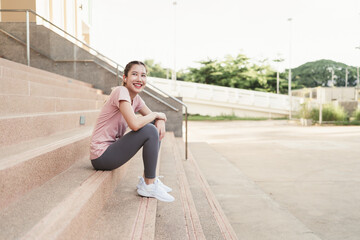 Happy Asian woman wearing sportswear rest sitting on stairs after exercise. Healthy exercise concept.