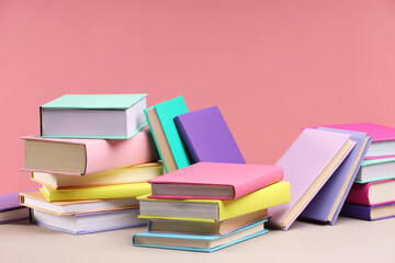 Many colorful books on beige table against pink background