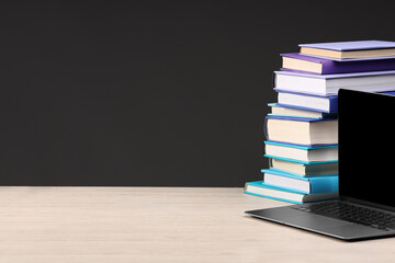 Stack of colorful books and laptop on white wooden table against black background, space for text