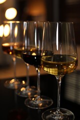 Different tasty wines in glasses on table against blurred lights, closeup
