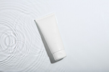 Cosmetic product. Tube with cream in water on light background, top view