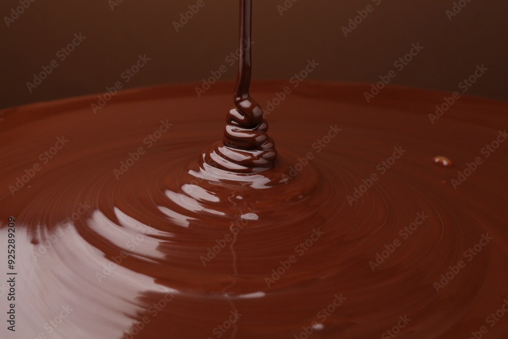 Poster Pouring delicious melted chocolate on brown background, closeup