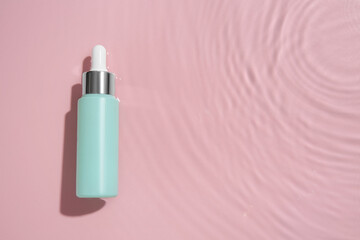 Bottle of cosmetic product in water on pink background, top view. Space for text