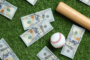 Baseball ball, bat and dollar banknotes on green grass outdoors, flat lay