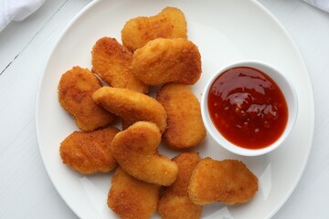 Tasty chicken nuggets with chili sauce on white table, top view