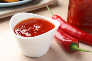 Spicy chili sauce in bowl on wooden table, closeup