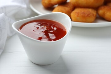 Spicy chili sauce in bowl on white wooden table, closeup