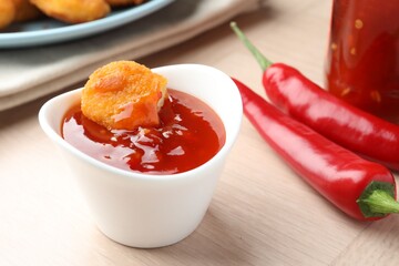 Chicken nugget into spicy chili sauce in bowl on wooden table, closeup