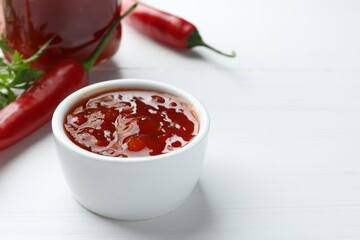 Spicy chili sauce in bowl on white wooden table, space for text