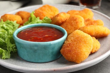 Plate with hot chili sauce, lettuce and nuggets on grey table, closeup