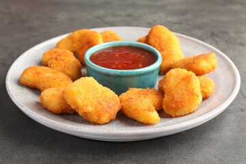 Plate with hot chili sauce and nuggets on grey textured table, closeup