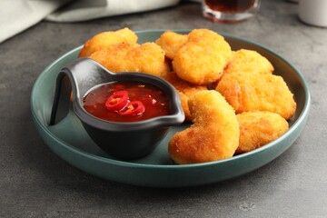 Plate with hot chili sauce and nuggets on grey textured table, closeup
