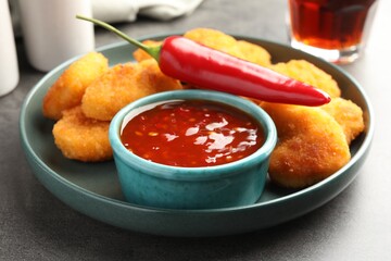 Plate with hot chili sauce, pepper and nuggets on grey textured table, closeup