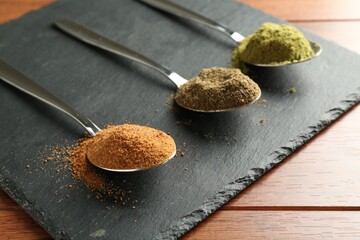 Different superfood powders in spoons on wooden table, closeup