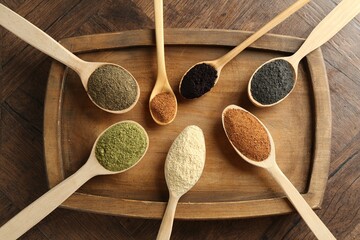 Different superfood powders in spoons on wooden table, top view