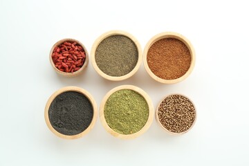 Different superfood powders and goji berries in bowls on white background, flat lay