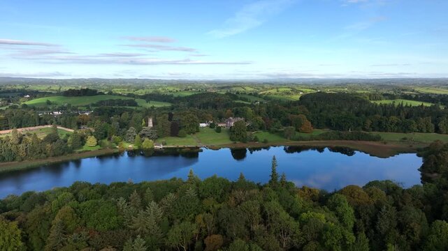 Castle Leslie, Glaslough, County Monaghan, Ireland, September 2022. Drone orbits clockwise gradually pushing across the lake towards the Walled Garden and St. Salvator's Church of Ireland.