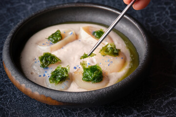 Crop person with spoon and cream soup with scallop