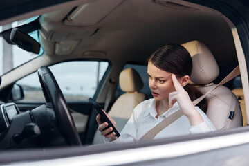 Woman in car, driver's seat, holding cell phone, looking at screen